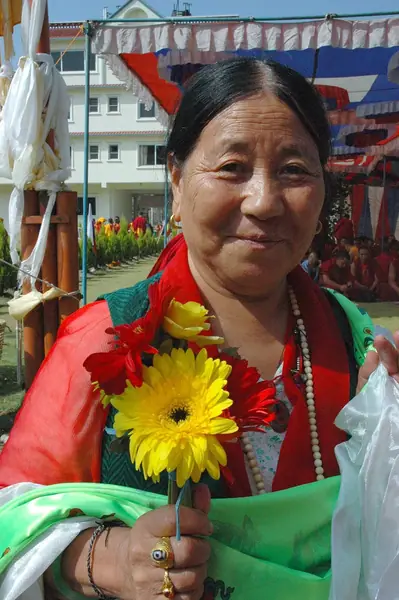 Tibetan Woman with flower and katag offerings, wearing a dZi stone ring, memorial wrist bracelet to Tibetan prisoners, and mala, Tharlam Monastery Courtyard, Boudha, Kathmandu, Nepal