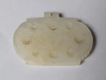 Amulet, generally oval, white nephrite jade, engraved with floral design and cavities for inset stones, India