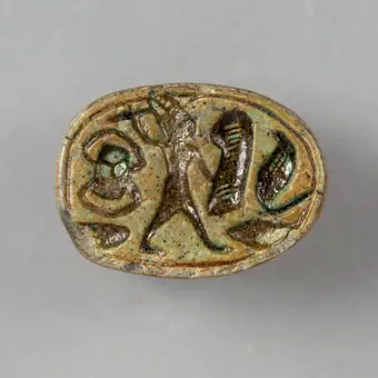 Amuletă sigiliu având partea superioară sculptată în forma unui scarabeu. Baza este decorată prin gravare cu următoarele elemente iconografice: scarabeu, zeitate cu suliță și scut, cobră. Pe margine c